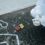 Forensic investigator examines crime scene outline on asphalt in protective suit.